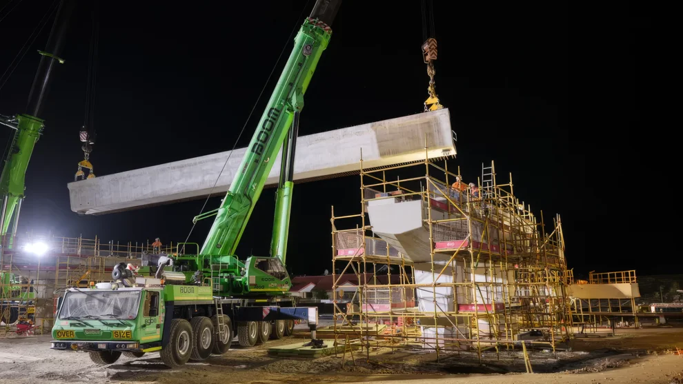 Two cranes lifting a long precast concrete beam onto a scaffolded pier at night during construction of Perth’s elevated Armadale Line